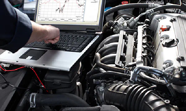Laptop over car engine, mechanic working.